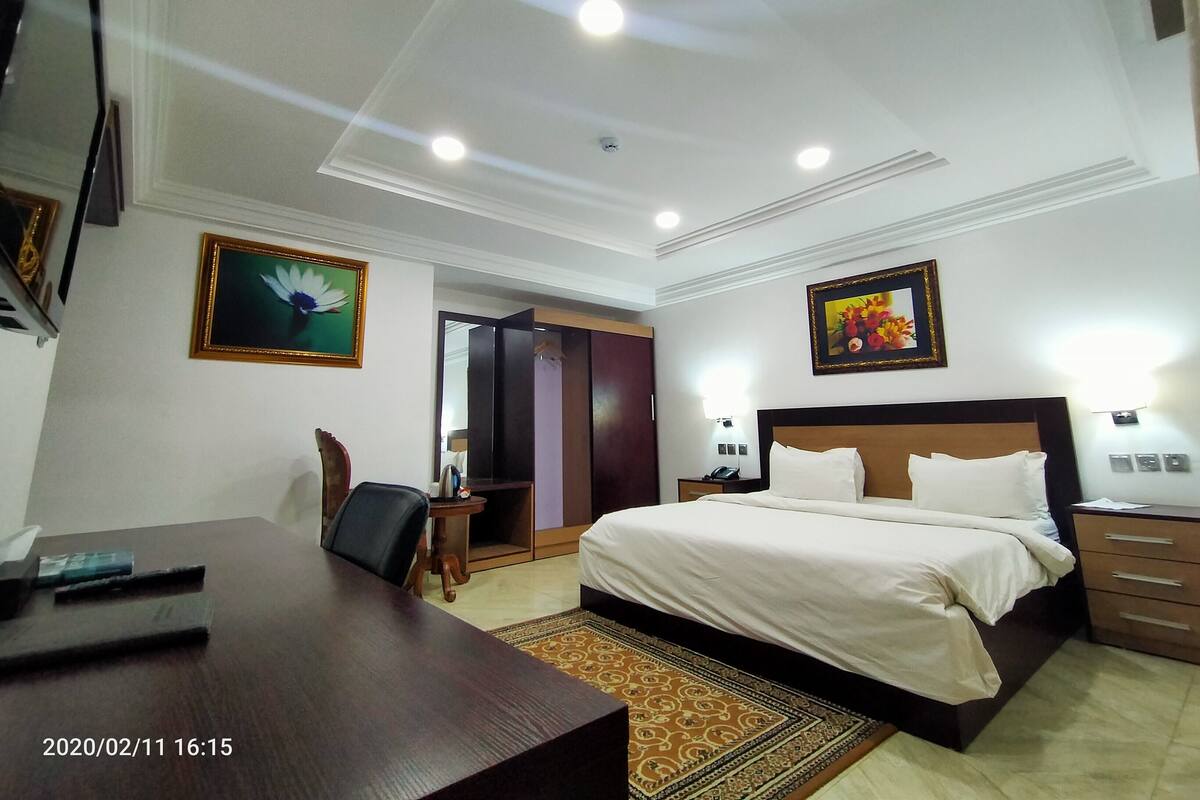 A hotel room with a bed, bedside tables, a desk, and a chair. There are two framed pictures on the walls.