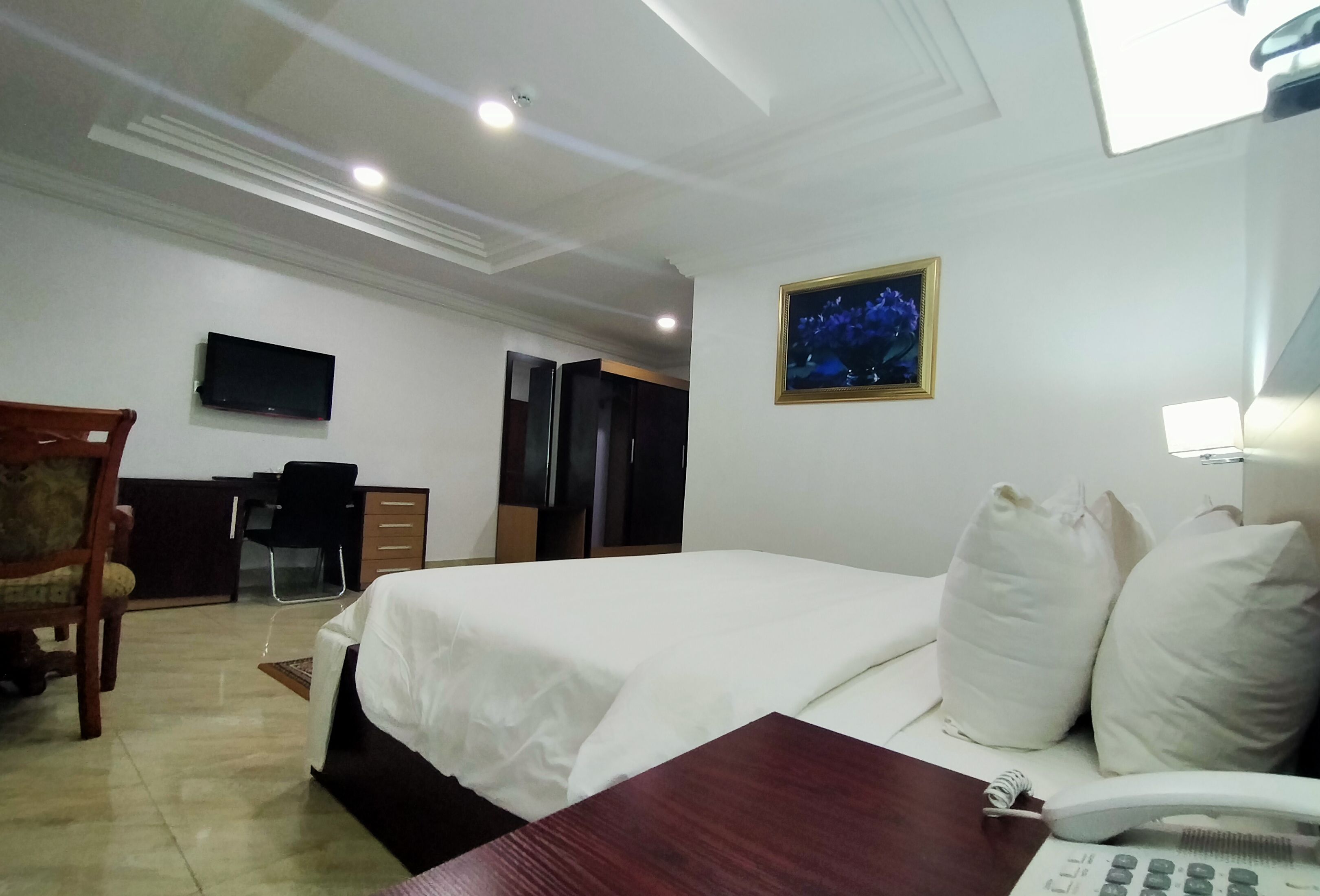 A hotel room with a bed, a desk, a chair, a television, a phone, and a picture on the wall.