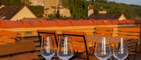 A table set for four with wine glasses, water glasses, and cutlery, overlooking a castle and forest.