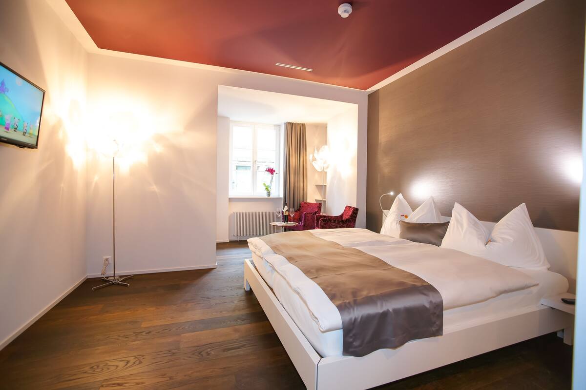 A modern hotel room with a large bed, a desk, and a view of the city.