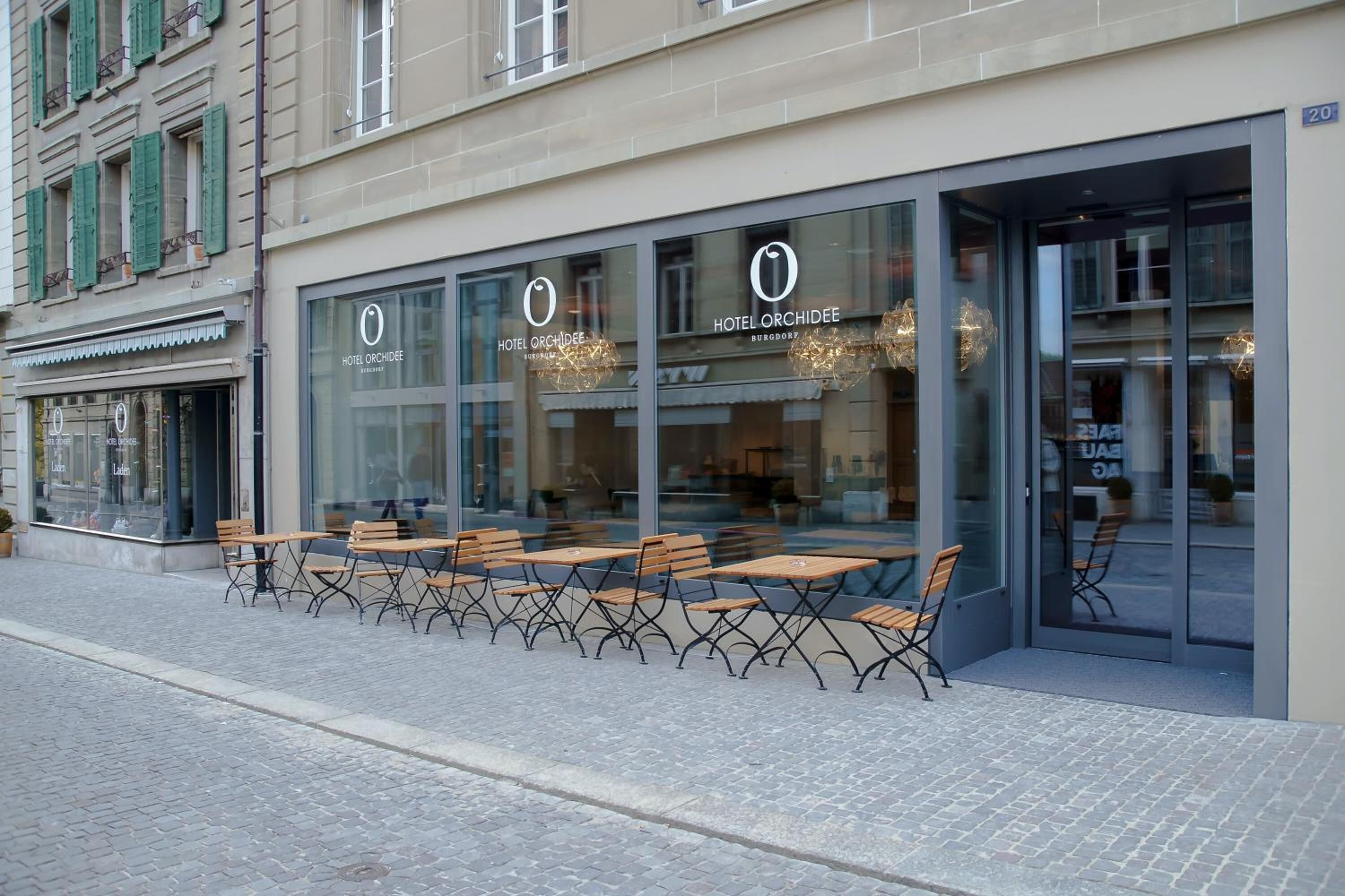 Exterior de un hotel con asientos al aire libre y grandes ventanales.