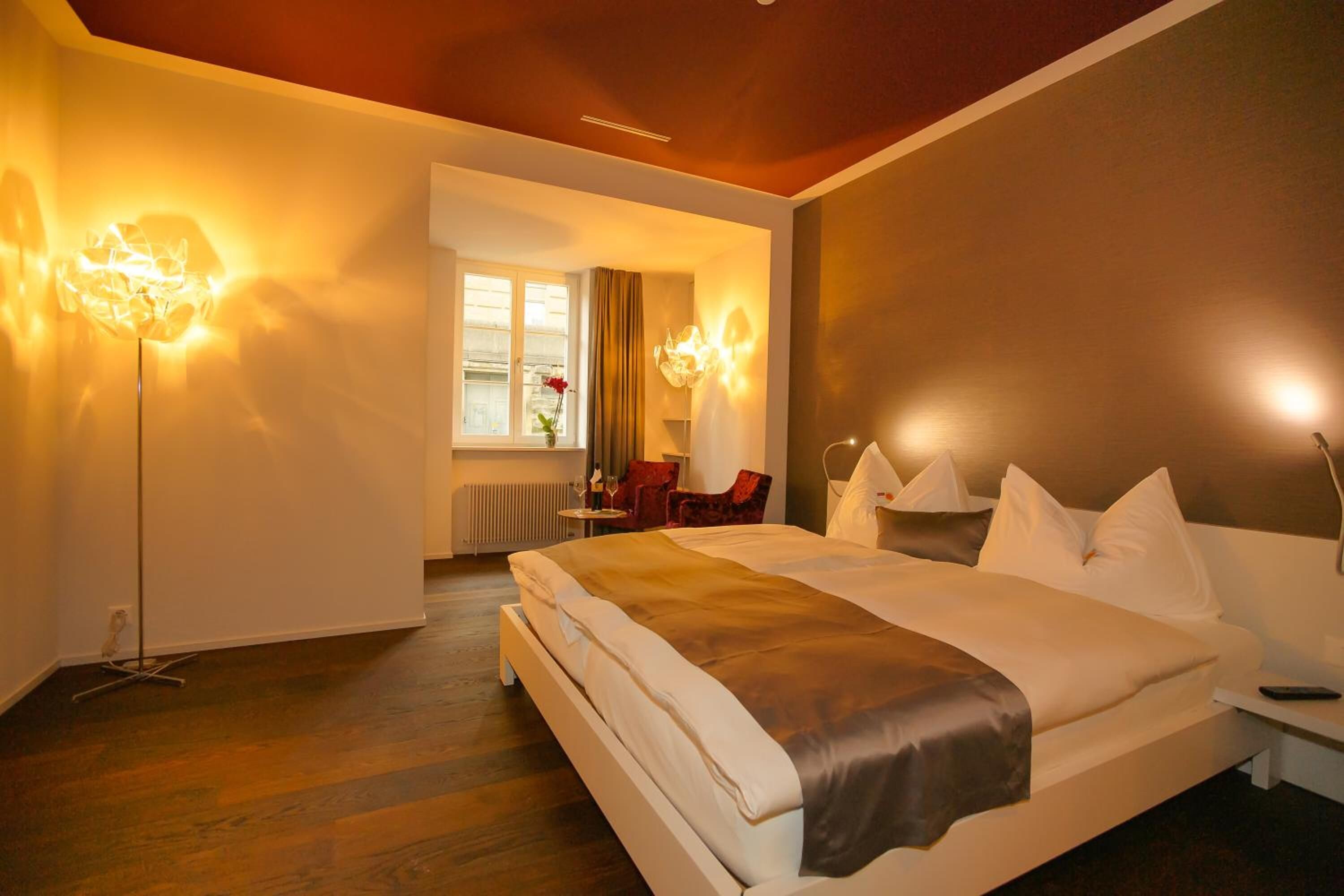A modern hotel room with a large bed, bedside tables, a desk, and a window with curtains.