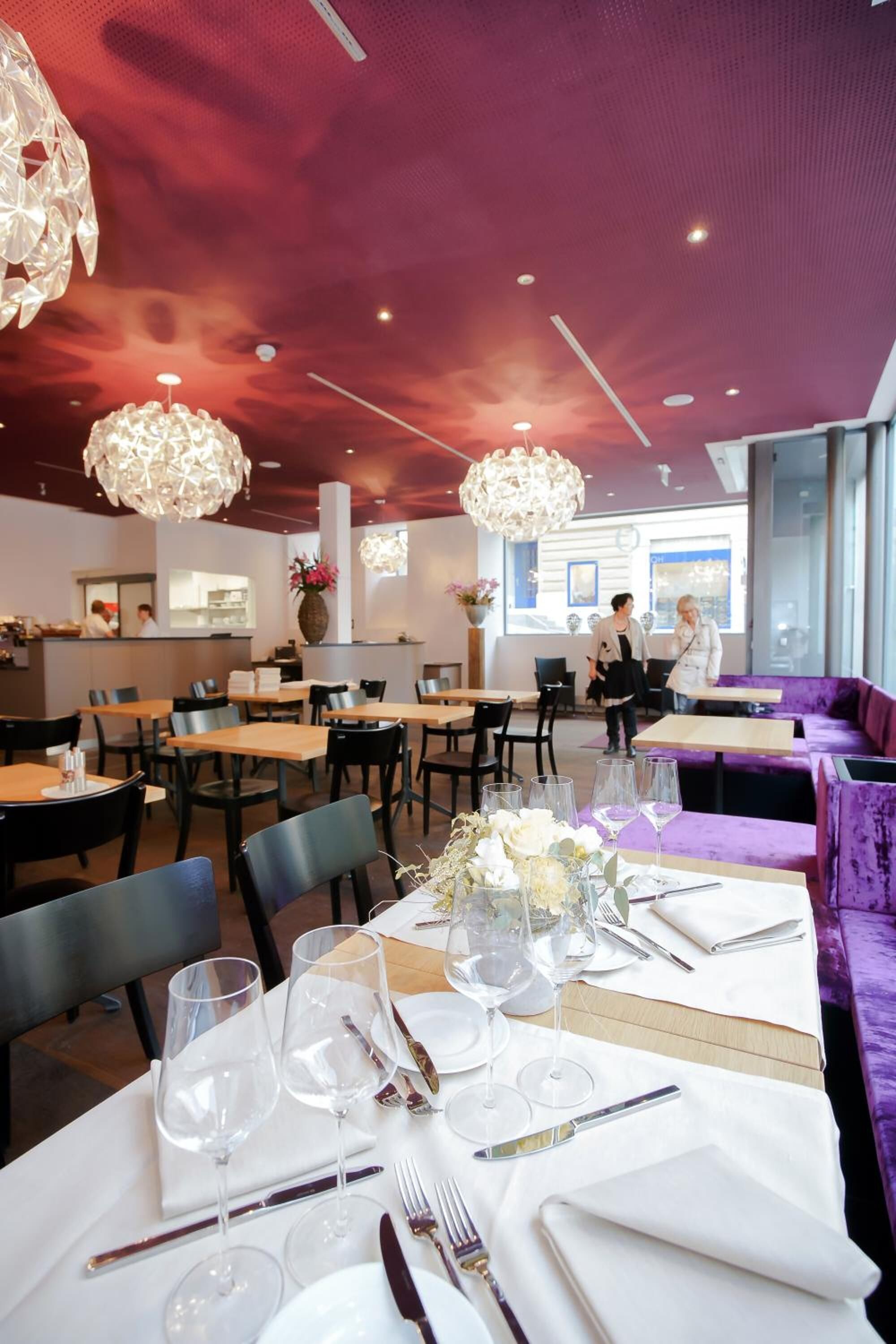 Un restaurante con asientos morados, mesas blancas y candelabros de cristal colgantes.