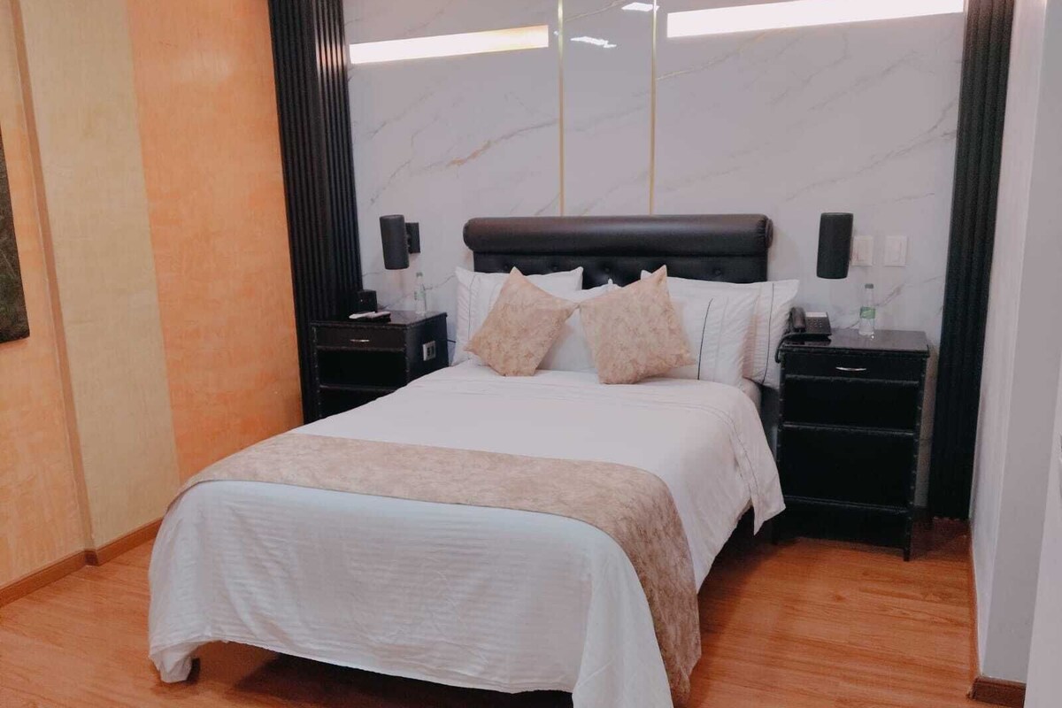 A neatly arranged hotel room with a large bed, two bedside tables, and a marble-patterned wall.
