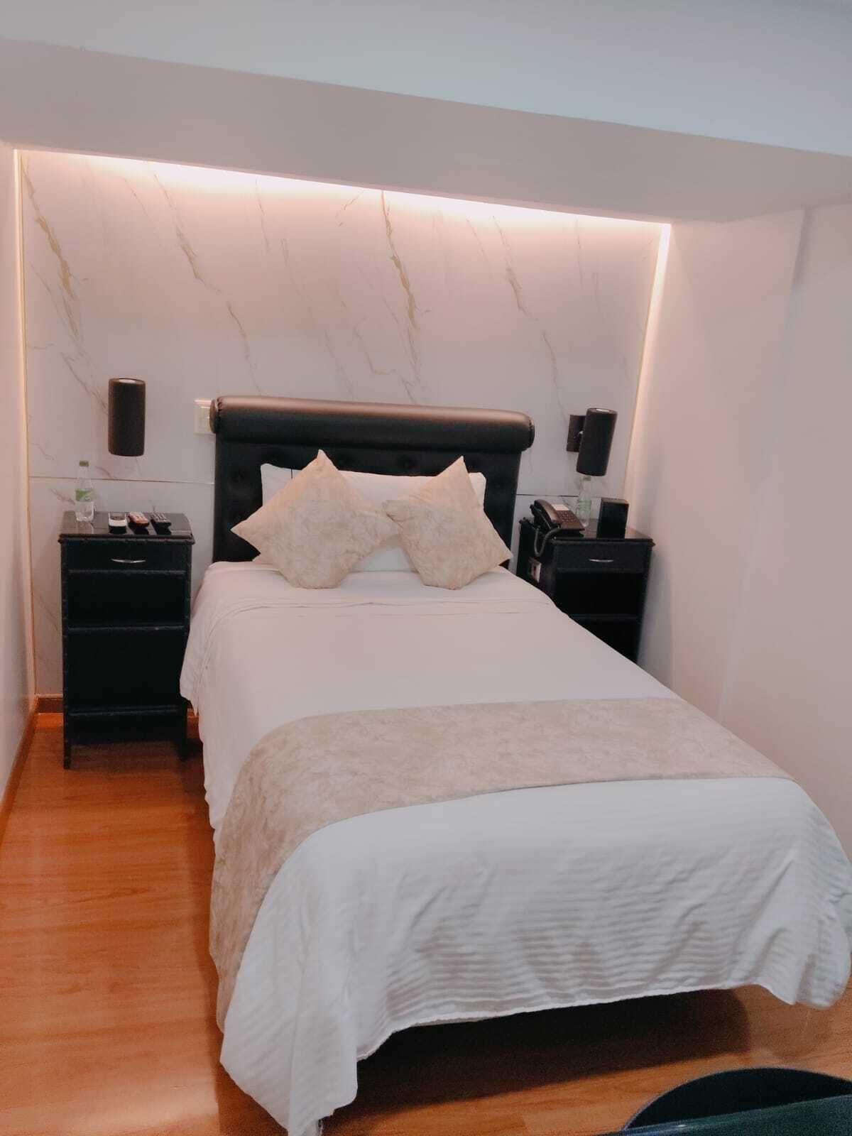 A bedroom with a bed, two bedside tables, a wall-mounted light, and a marble wall.