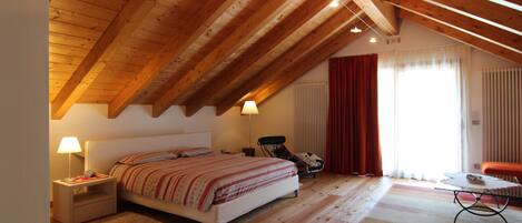 A bedroom with a wooden ceiling, a bed, a nightstand, a chair, a table, and a window with curtains.