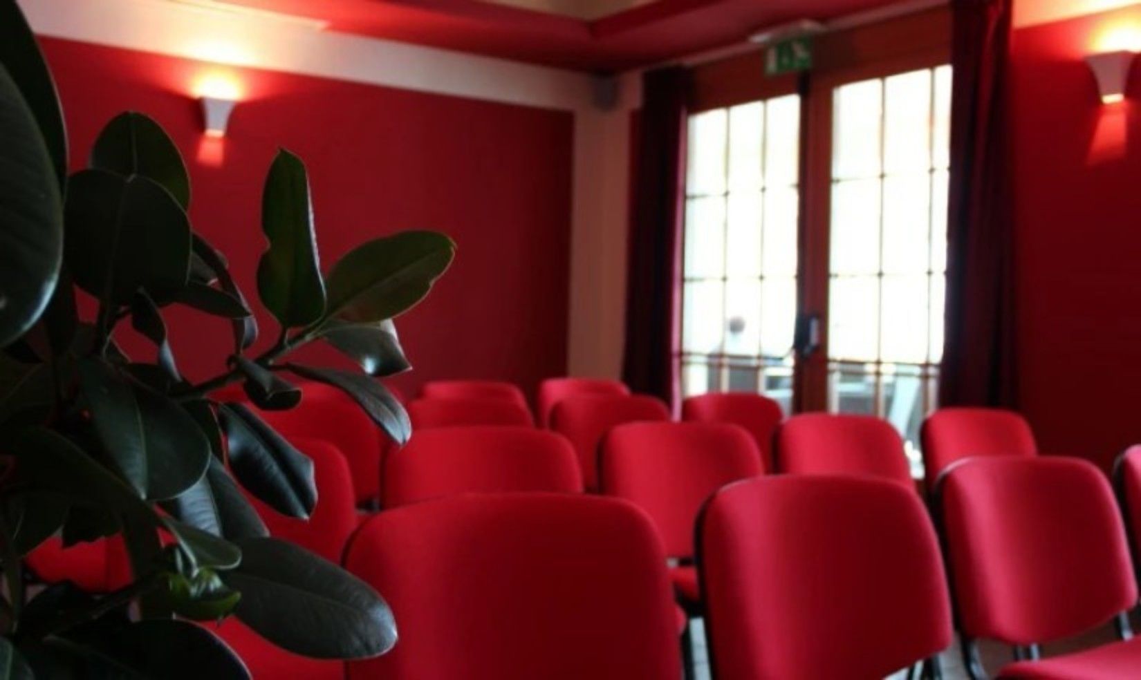 A room with red walls, a large window, and several red chairs arranged in rows.