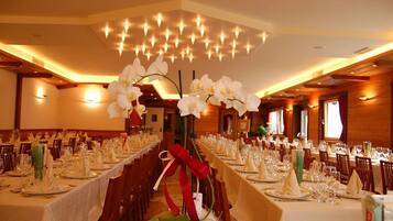 Une salle de banquet avec de longues tables dressées pour le repas, agrémentée d’orchidées blanches et d’un centre de table composé d’un ruban rouge.