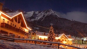 A snow-covered mountain town at night with illuminated buildings and a snow-covered tree in the foreground. - Albergo Edelweiss (Crodo)