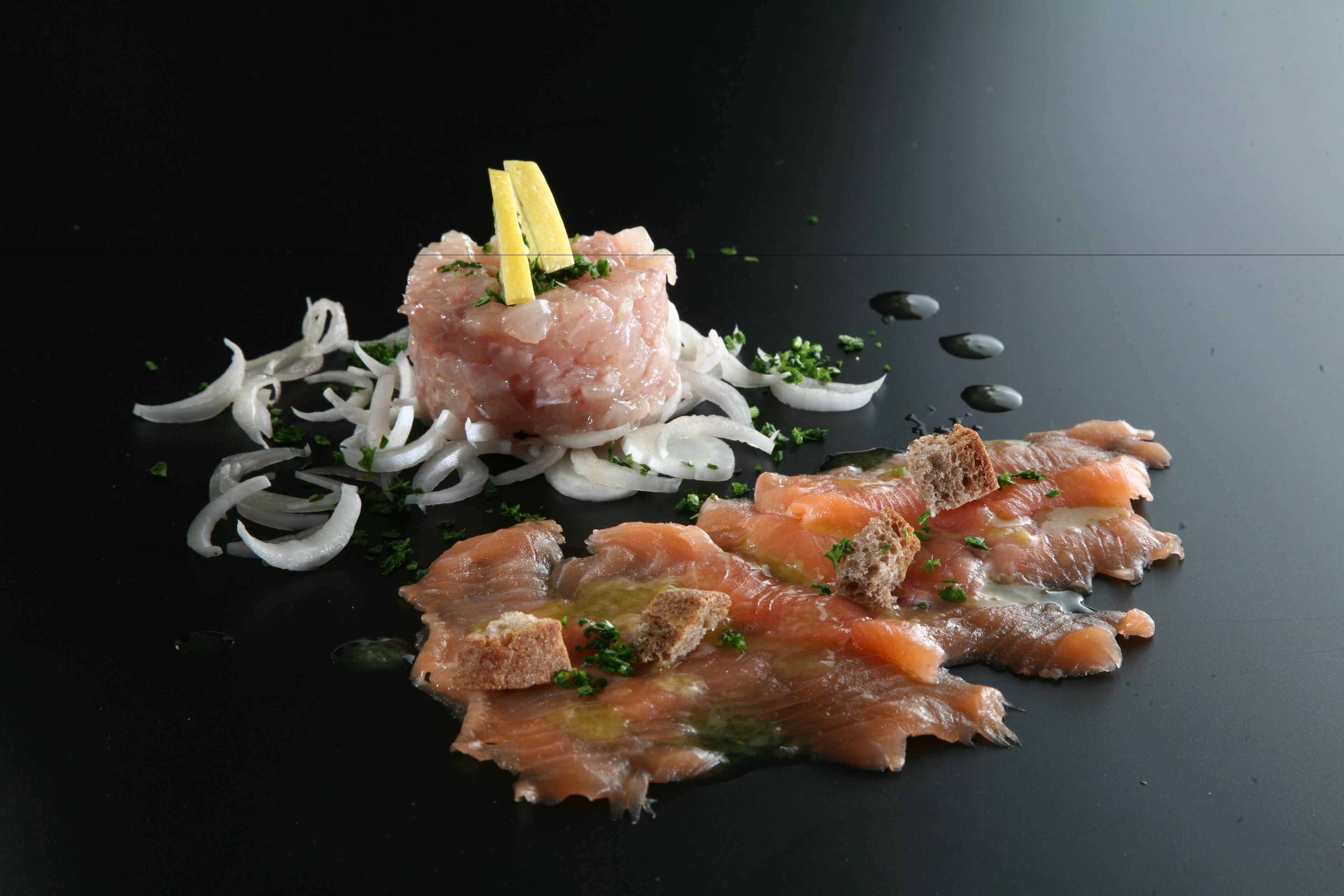 A dish with raw fish, onions, and bread on a dark surface.
