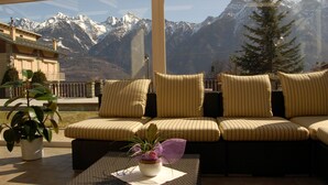 A sunlit room with a sofa facing a mountain view. - Albergo Edelweiss (Crodo)
