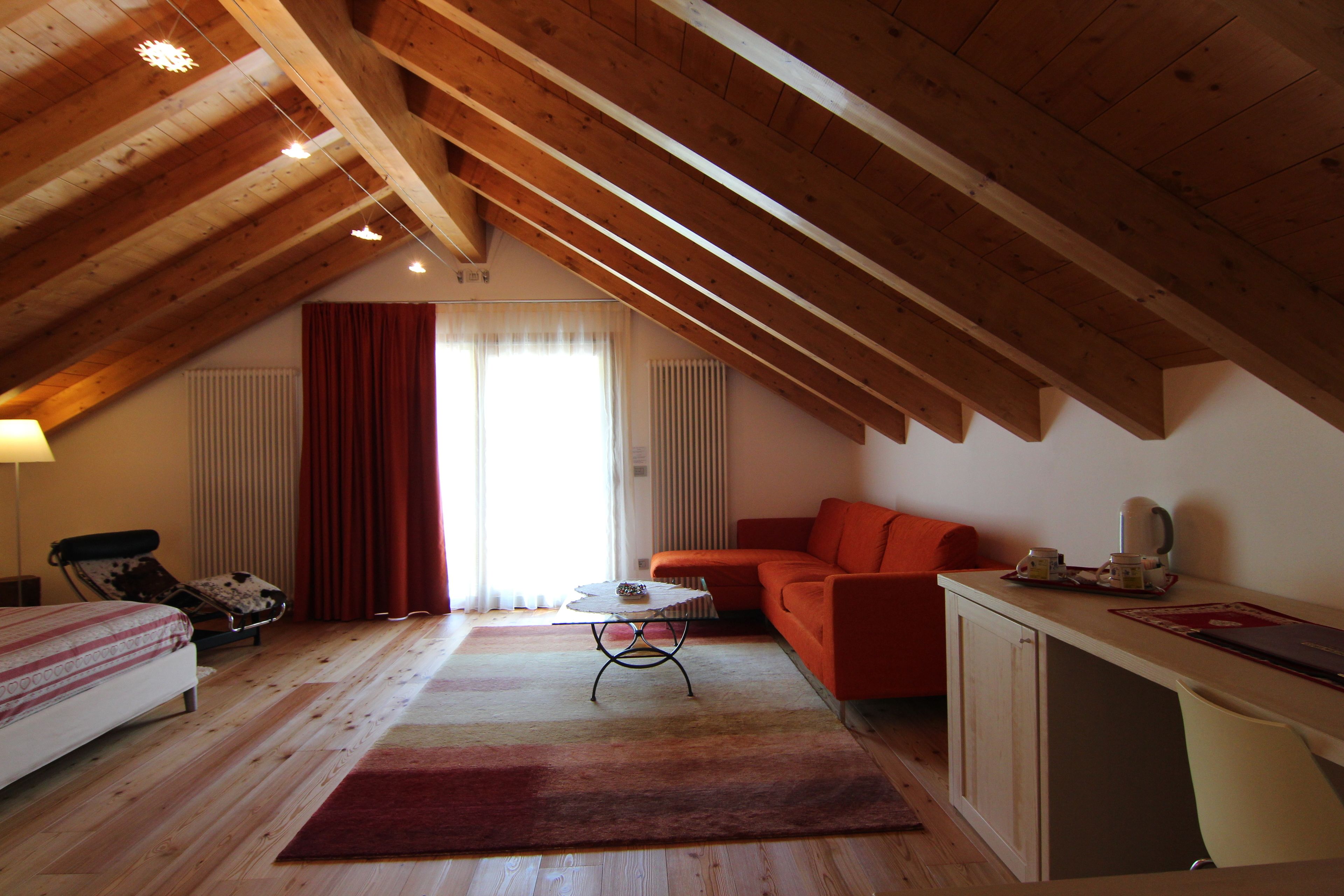 Una stanza con soffitto a falde, un letto, un divano, un tavolino e un termosifone.