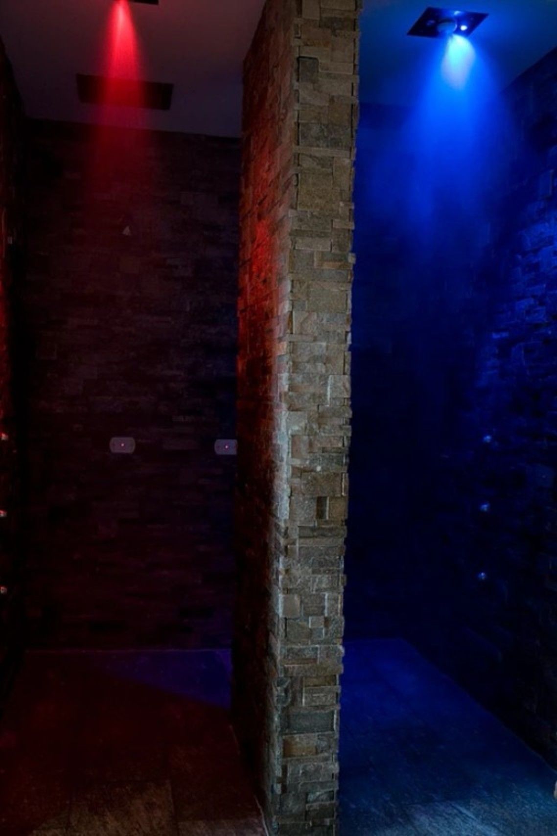 Un pasillo estrecho con una pared de ladrillo a un lado y una pared iluminada en azul al otro.