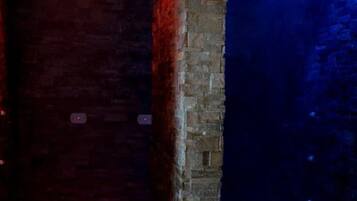 Un pasillo estrecho con una pared de ladrillo a un lado y una pared iluminada en azul al otro.