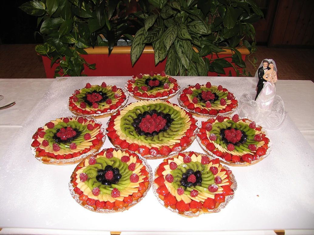 Ein Tisch mit sechs Obstkuchen, die kreisförmig angeordnet sind, einer kleinen Figur und einem Blumentopf im Hintergrund.