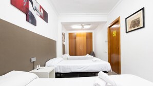A hotel room with two beds, a wooden wardrobe, a ceiling fan, and artwork on the walls. - Pensión Galicia (Canovelles)