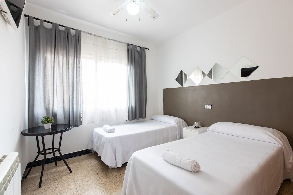 Een hotelkamer met twee enkele bedden, een tafeltje met een bloempot en een plafondventilator.