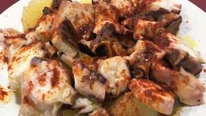 A plate of octopus with a reddish seasoning, served on a white plate. - Pensión Galicia (Canovelles)