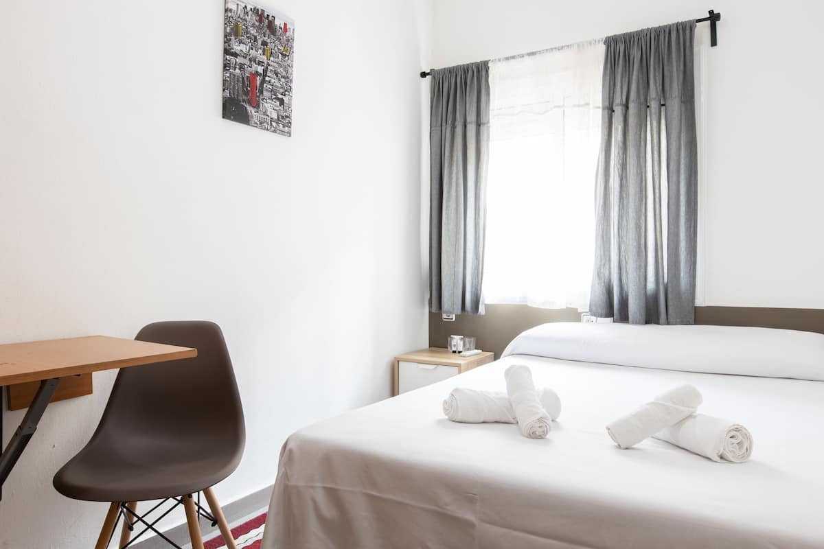 Een hotelkamer met een bed, een stoel, een klein tafeltje en een nachtkastje.