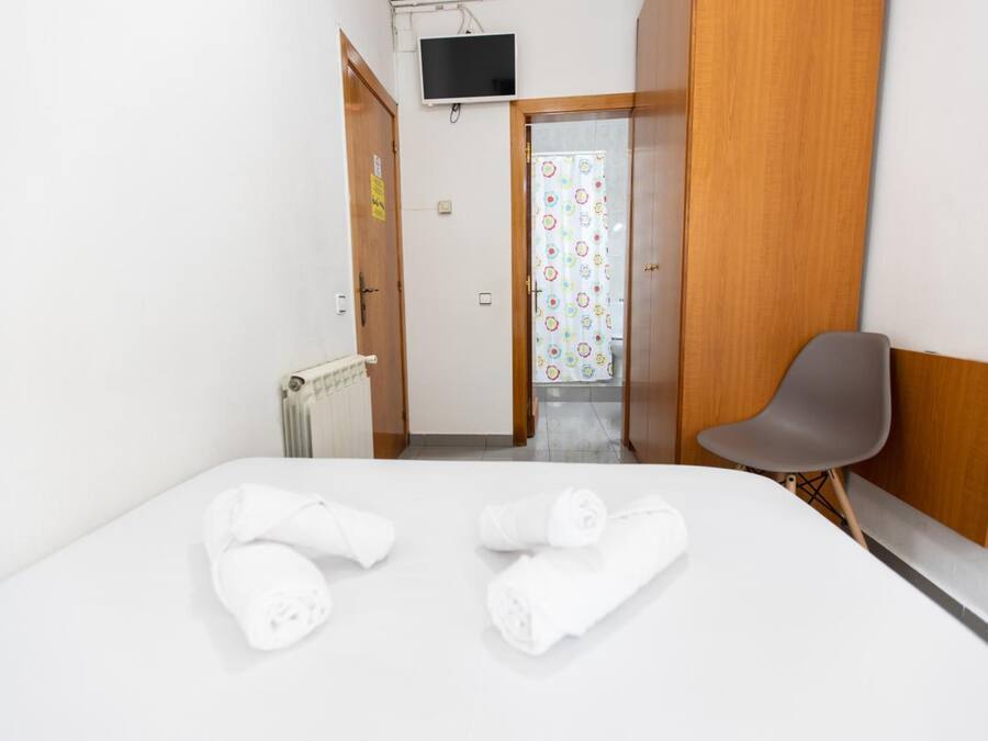 Habitación de hotel con cama, una silla, televisor y baño visible a través de una puerta abierta.