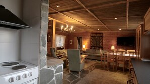 Interior rústico de una cabaña con chimenea de piedra, techo de madera y un comedor con sillas y mesa de madera.