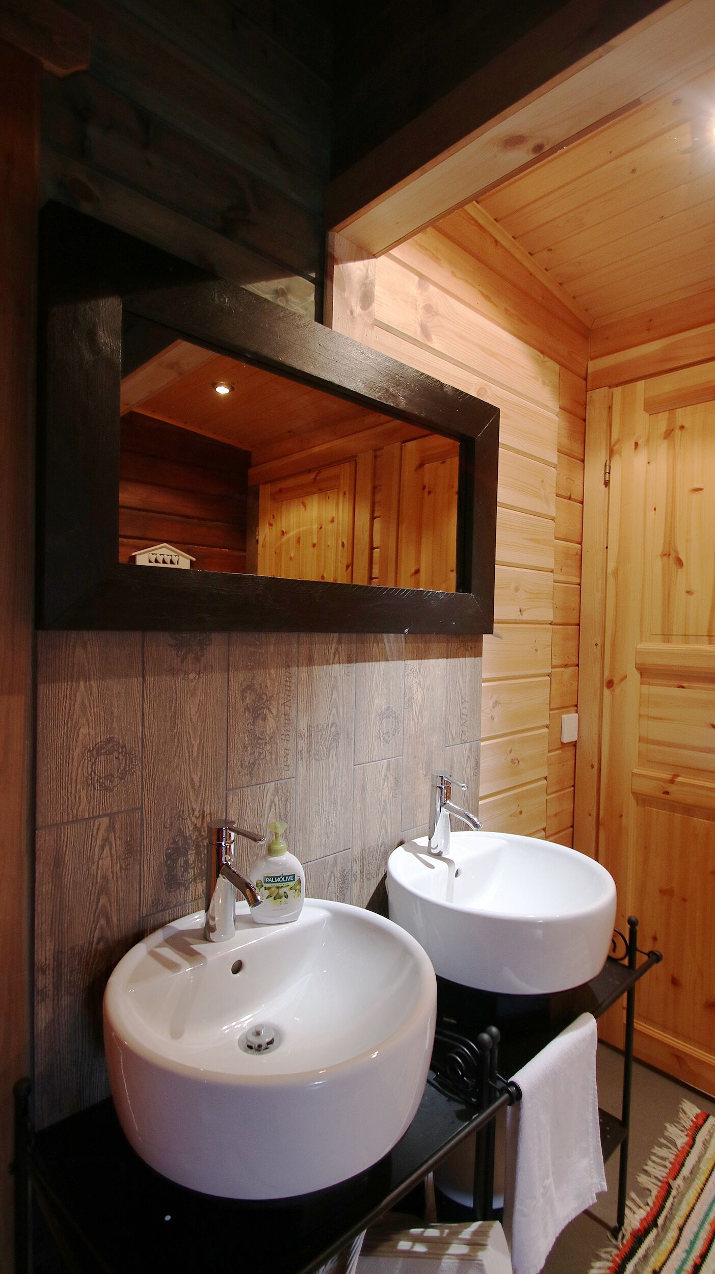 A bathroom with two white sinks, a mirror, and a small bottle of Palmolive soap.