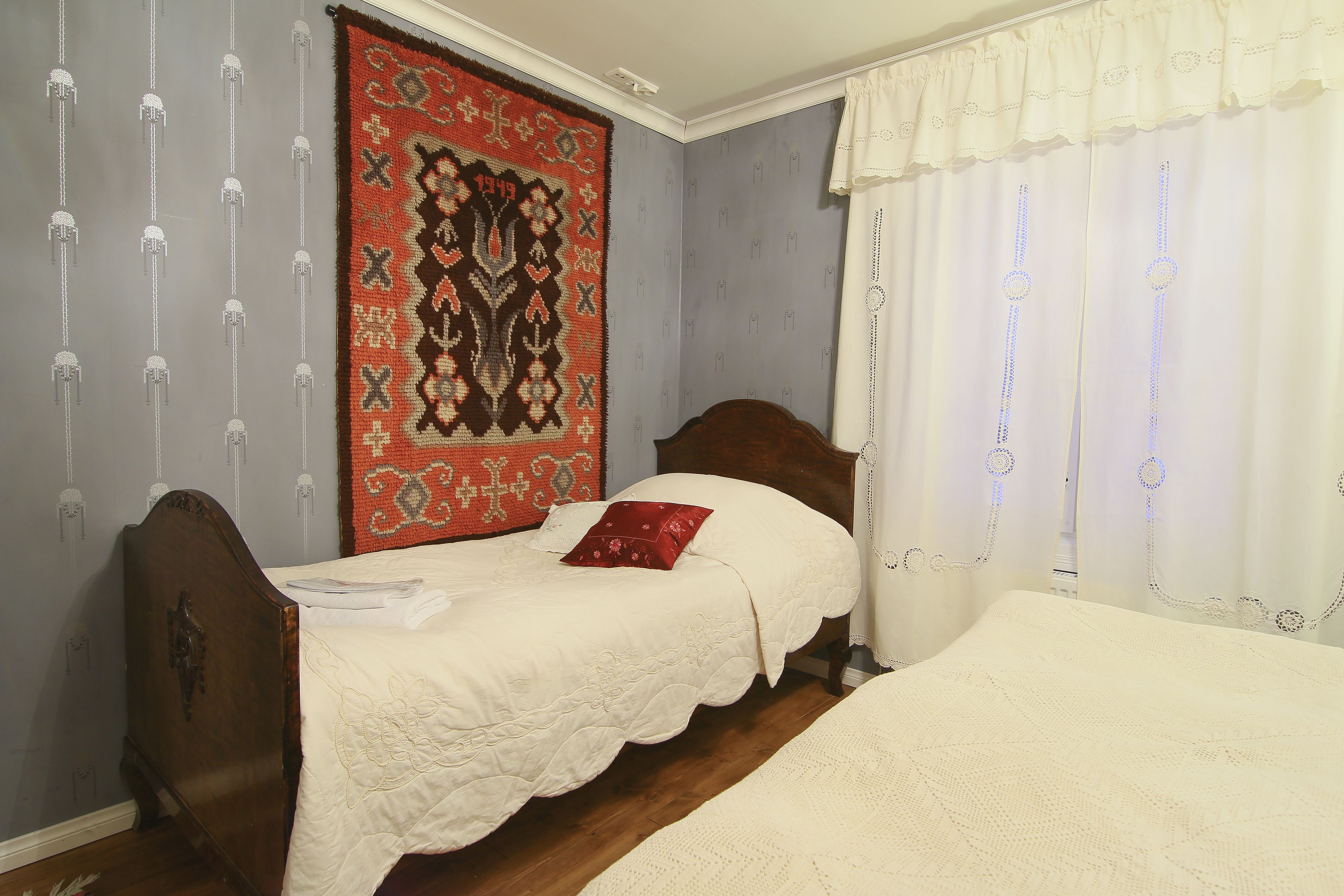 A bedroom with two single beds, a large patterned rug, and a window with curtains.