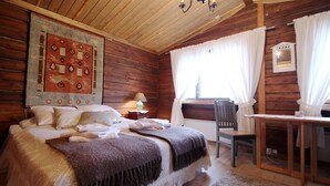 Acogedora habitación tipo cabaña de madera con cama, mesa, silla y ventana con cortinas.