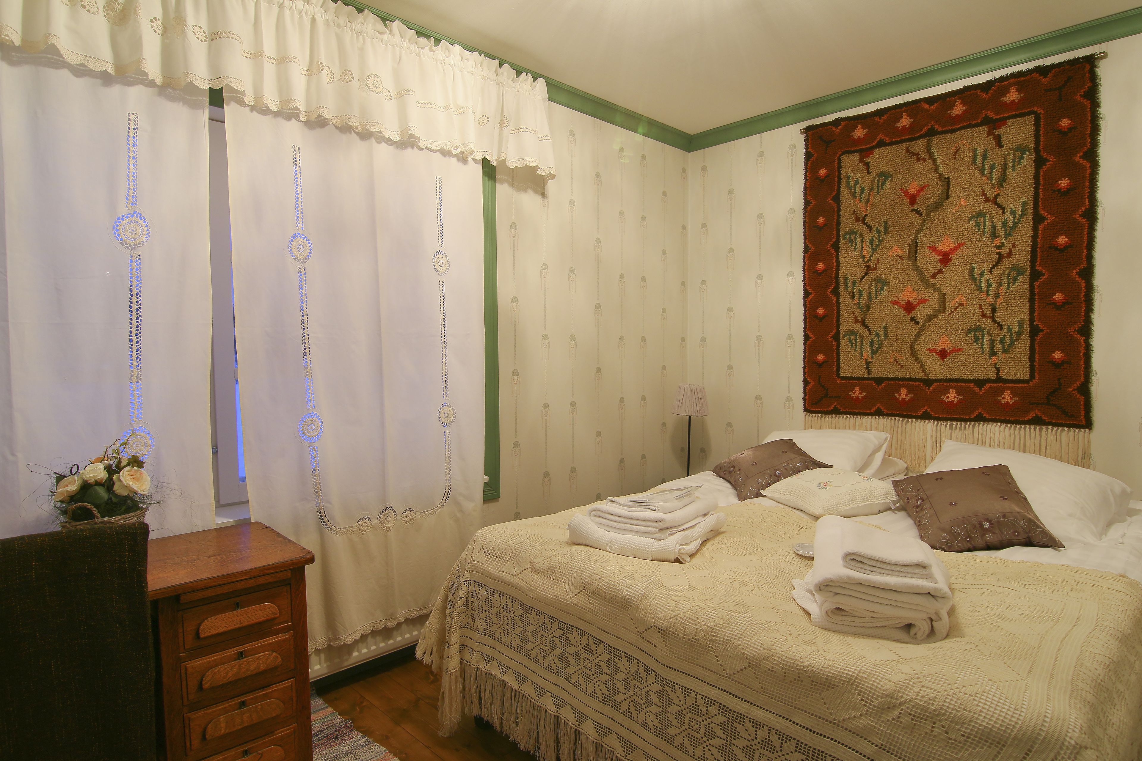 Un lit bien fait, avec des serviettes pliées, une commode en bois et une tapisserie décorative au mur.