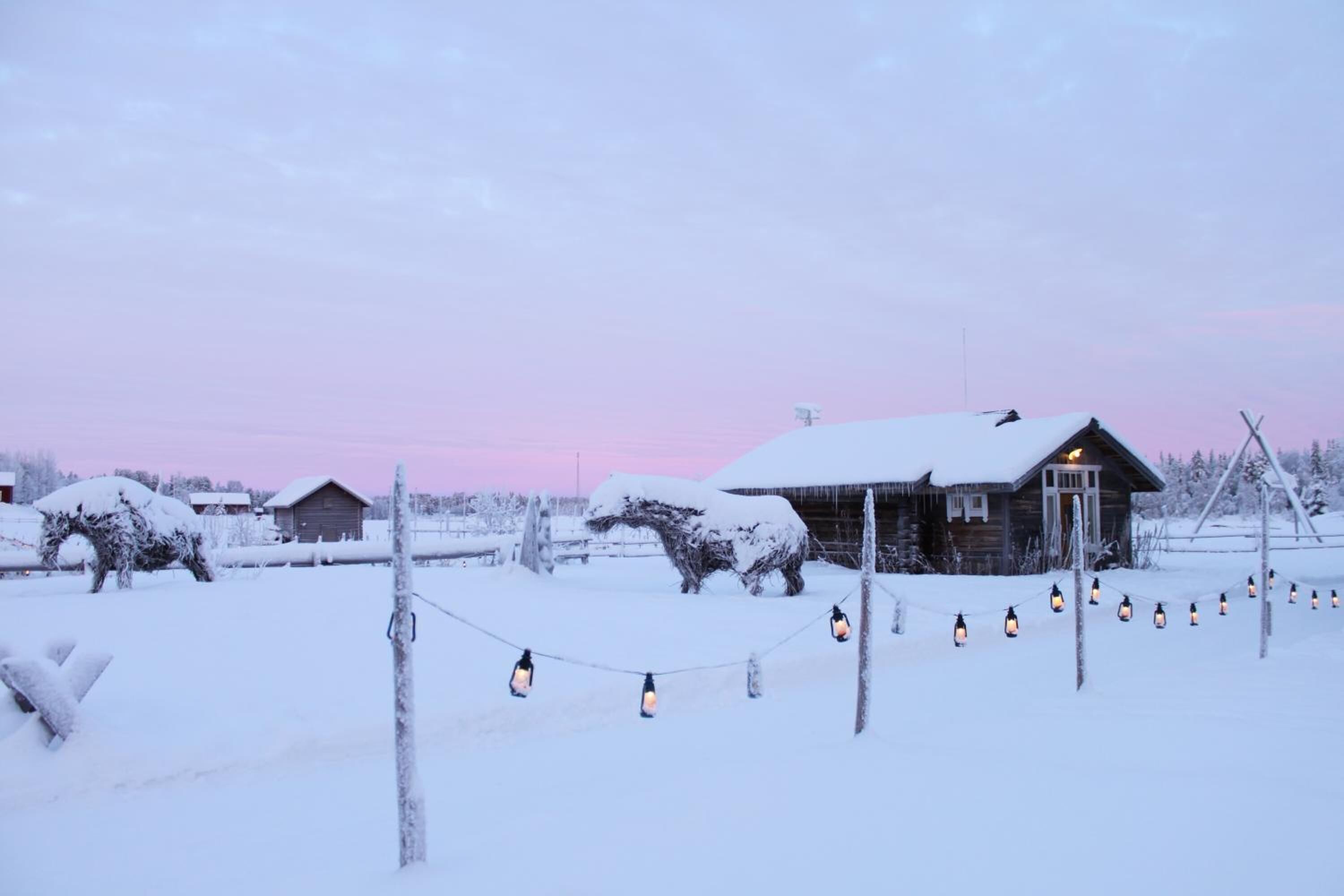 A snow-covered landscape with a wooden cabin and a string of lanterns.