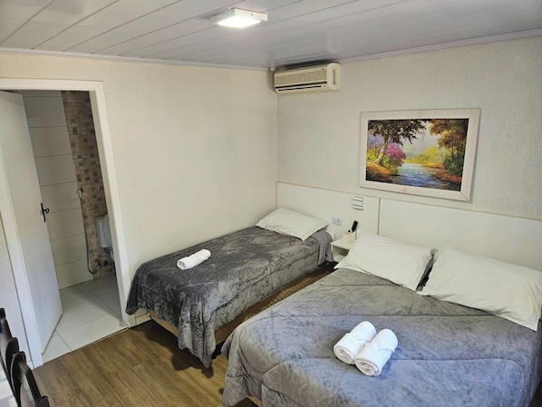 Une chambre d’hôtel avec deux lits, un espace douche, un tableau au mur et un appareil de climatisation.