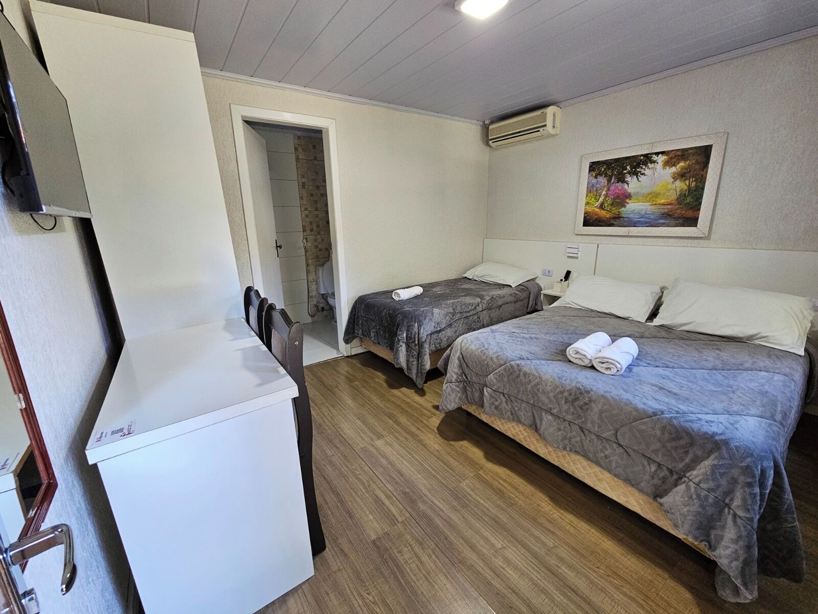 A hotel room with two beds, a small kitchenette, a shower area, and a painting on the wall.