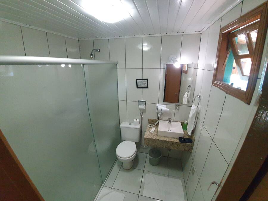 Uma casa de banho compacta com chuveiro em cabine de vidro, sanita, lavatório com espelho e uma pequena janela.