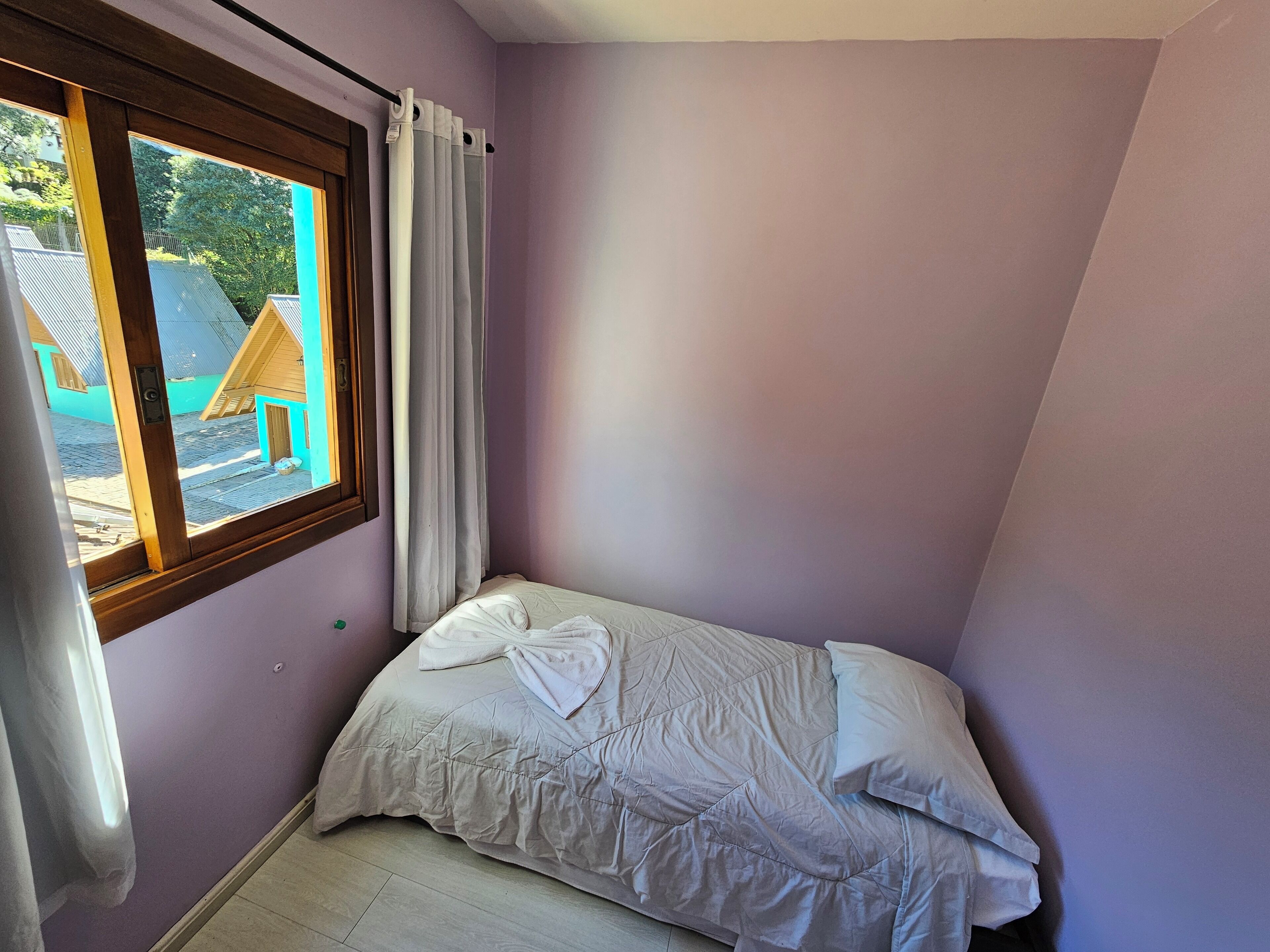 Una camera da letto piccola con un letto singolo, una finestra con tende e vista su un edificio.