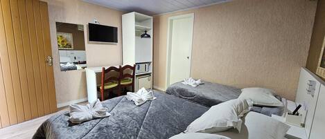 Habitación de hotel con dos camas, un escritorio, una silla, un televisor y un aire acondicionado.