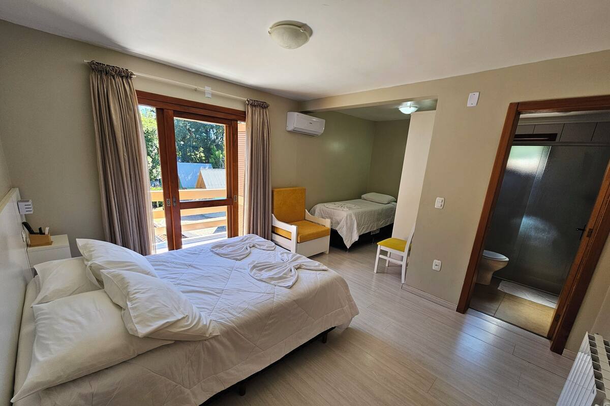 Un dormitorio con cama, una silla, una mesita y la puerta del baño.