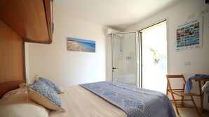 Une chambre à coucher avec un lit, une chaise, une porte vitrée donnant sur un balcon et une affiche accrochée au mur.