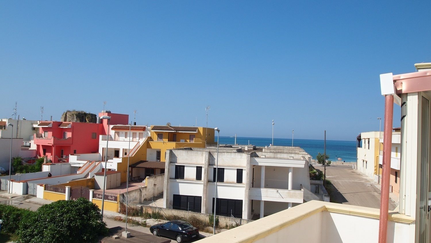 A coastal residential area with colorful buildings, a clear sky, and a view of the sea.