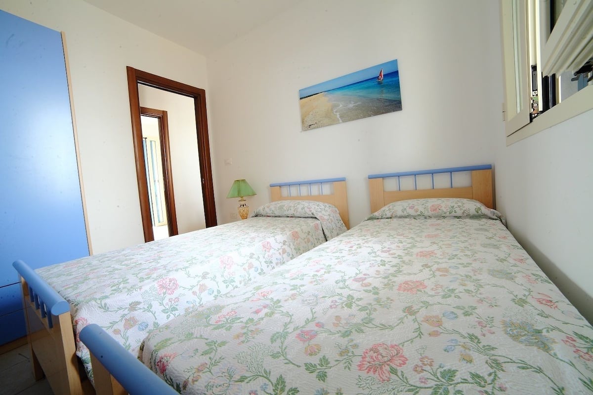 Un dormitorio con dos camas, un cuadro de una playa y una ventana con cortinas.