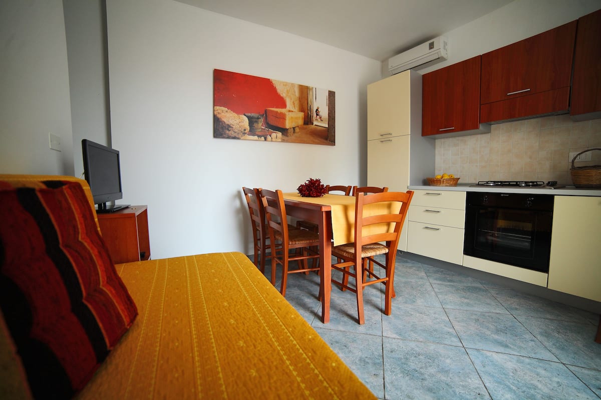 Una cocina compacta con armarios de madera, una mesa de comedor con sillas, un sofá y un cuadro en la pared.
