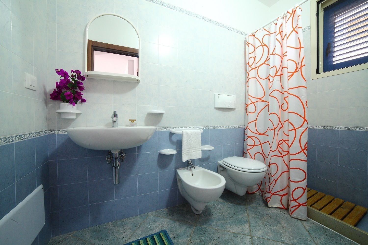 A bathroom with a sink, bidet, toilet, and a shower curtain.