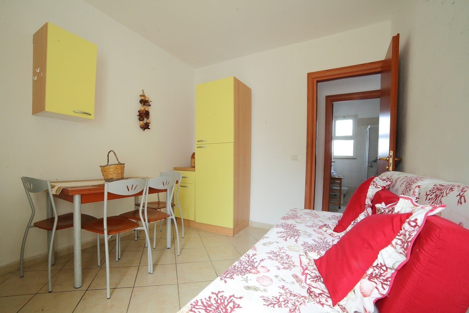 Una habitación pequeña y luminosa con una cama, un escritorio y sillas. Hay una ventana y una puerta.
