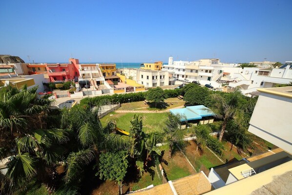 Zona residencial con un patio central rodeado de edificios, vista despejada al mar y palmeras.