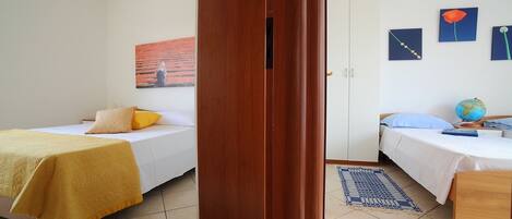 A room with two beds, a wooden door, a globe on a nightstand, and artwork on the wall.