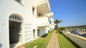 Un chemin mène à un bâtiment blanc doté de fenêtres grillagées et bordé d’un petit jardin.
