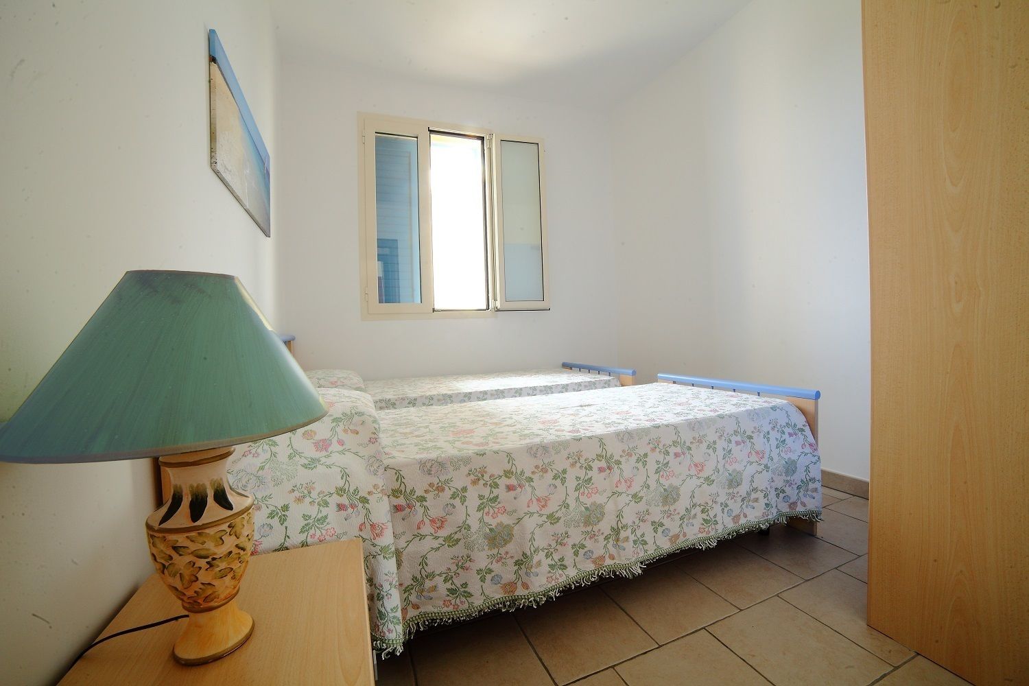 A small bedroom with a single bed, a nightstand, a lamp, and a window.