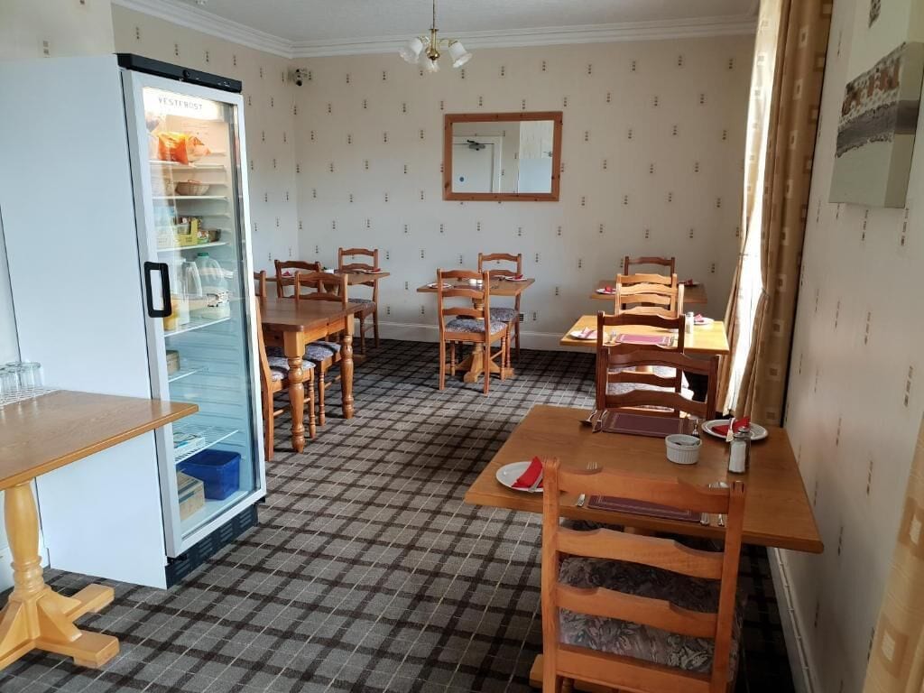 A dining area with a checkered floor, wooden tables and chairs, a refrigerator, and a mirror on the wall.