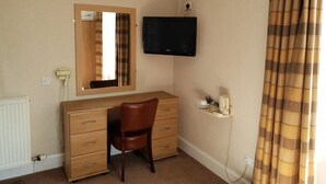 A room with a wooden desk, a chair, a television mounted on the wall, and a radiator.
