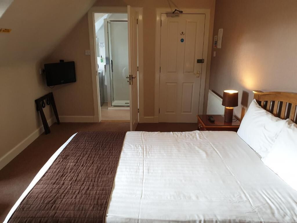 A hotel room with a bed, a bedside lamp, a television mounted on the wall, and a door leading to a bathroom.