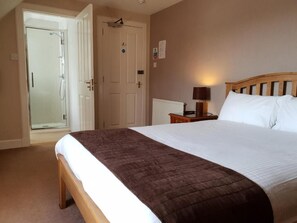 A hotel room with a bed, a bedside table with a lamp, a door leading to a shower, and a radiator.